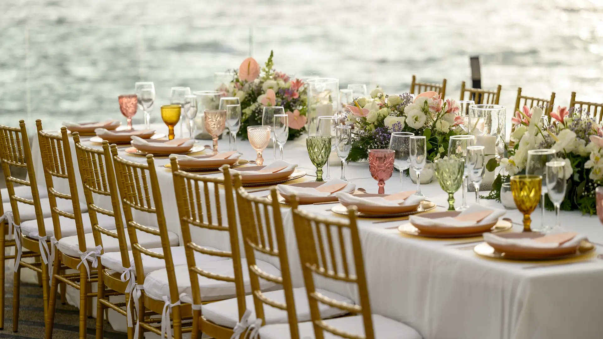 A long celebration table set with flowers and colored glass on the ocean terrace.