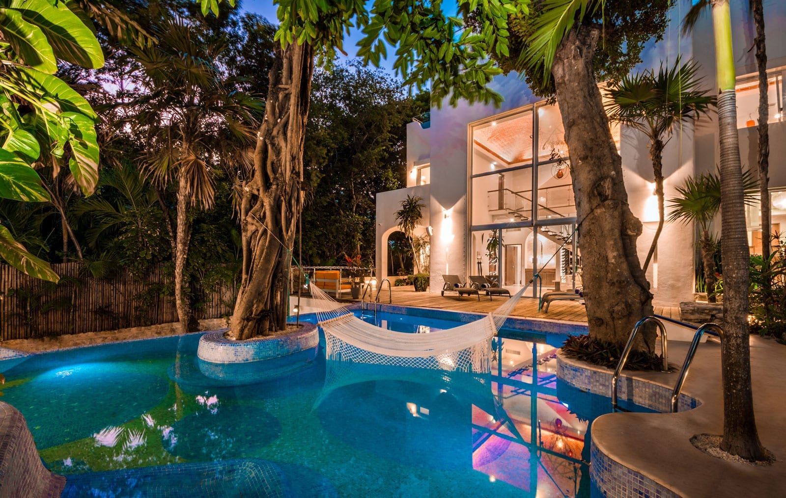 Exterior view of Casa Los Charcos in Playacar Phase 1, highlighting its pristine swimming pool and surrounded by lush tropical vegetation.
