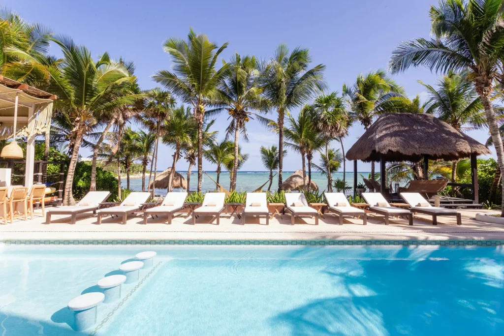 Hacienda Caracol pool with in-water stools, sun loungers, palms and ocean beyond — Tulum, Mexico
