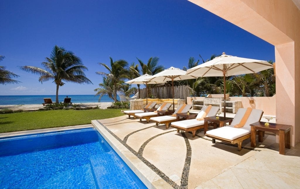 Villa Palmilla poolside loungers beneath umbrellas facing the lawn, palms and sea — Akumal, Mexico