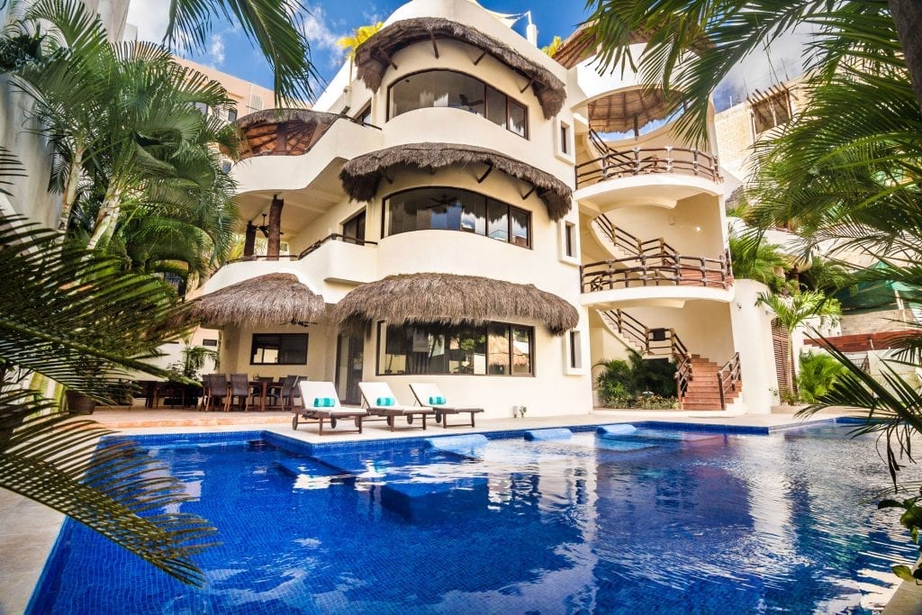 Villa Mirasol three-story facade with thatched balconies above the pool — Playa del Carmen, Mexico