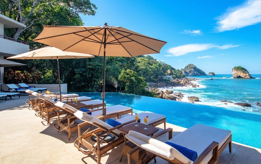 Villa Kismet wood-framed loungers and umbrellas along the oceanfront pool — Puerto Vallarta, Mexico