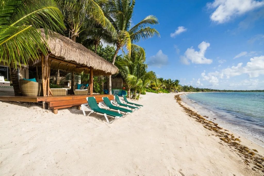 Villa Moonstar thatched beach shade with green loungers by the water — Tulum, Mexico