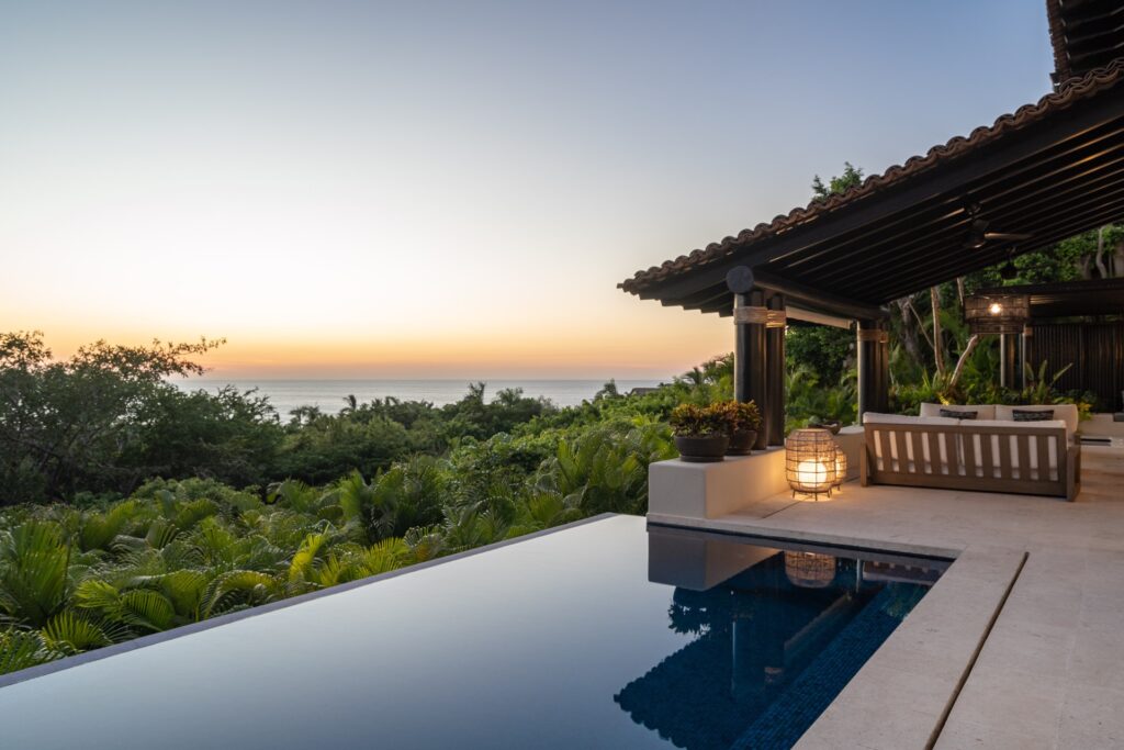 Villa Diez Four Seasons pool at dusk beside a lantern-lit covered terrace and treetops — Punta Mita Nayarit, Mexico