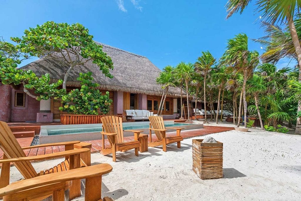 Casa Cantarena villa exterior with wooden chairs on the sand and swimming pool — Tulum, Mexico