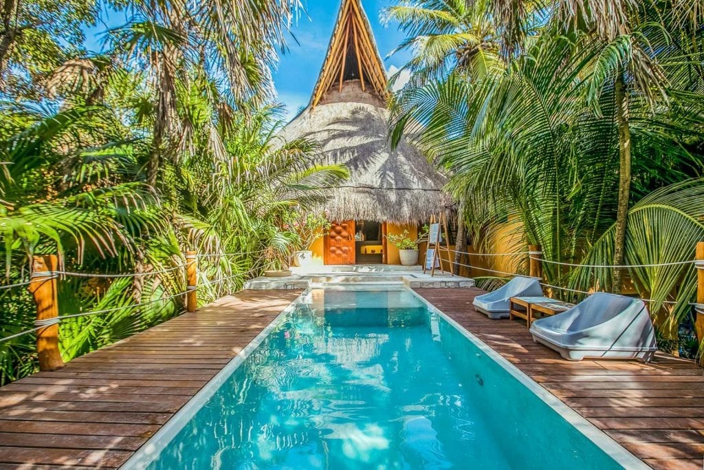 Casa Nalum pool with wood deck, loungers and thatched villa behind — Tulum, Mexico