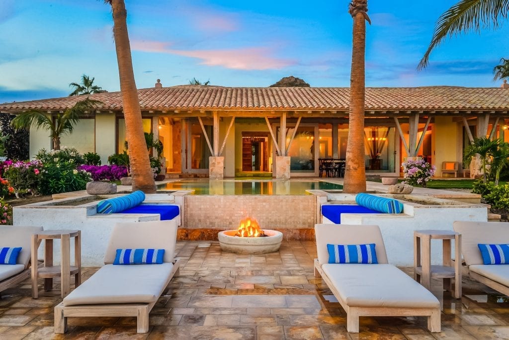 Villa Piedra Blanca fire pit between loungers with the lit villa beyond at dusk — Los Cabos, Mexico