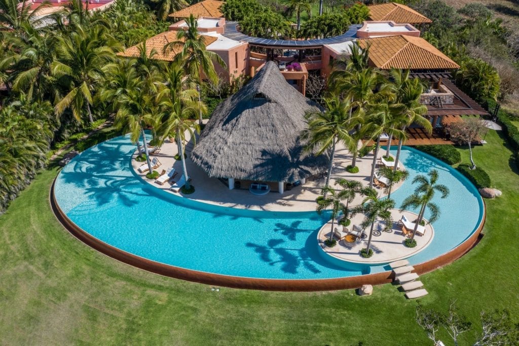 Aerial view of a circular pool surrounding a thatched pavilion and palm trees