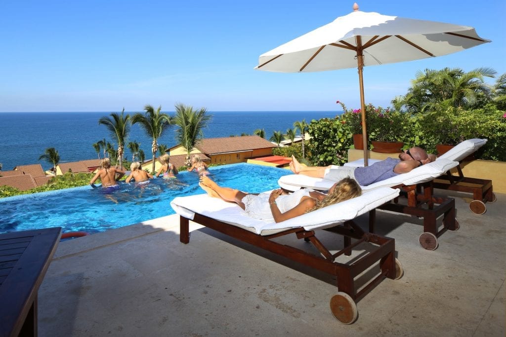 Four Seasons Twin Villas people on poolside loungers beneath a white umbrella — Punta Mita Nayarit, Mexico