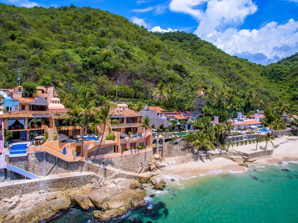 Villa Azul Celeste coastal buildings beside a beach, rocky shore and steep green hill — Puerto Vallarta, Mexico
