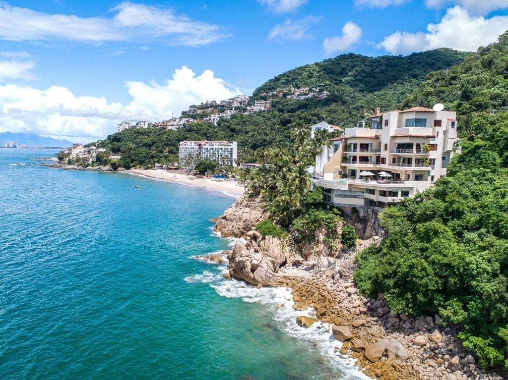 Villa Bahia aerial along the shore, the villa rising at the rocky point — Puerto Vallarta, Mexico