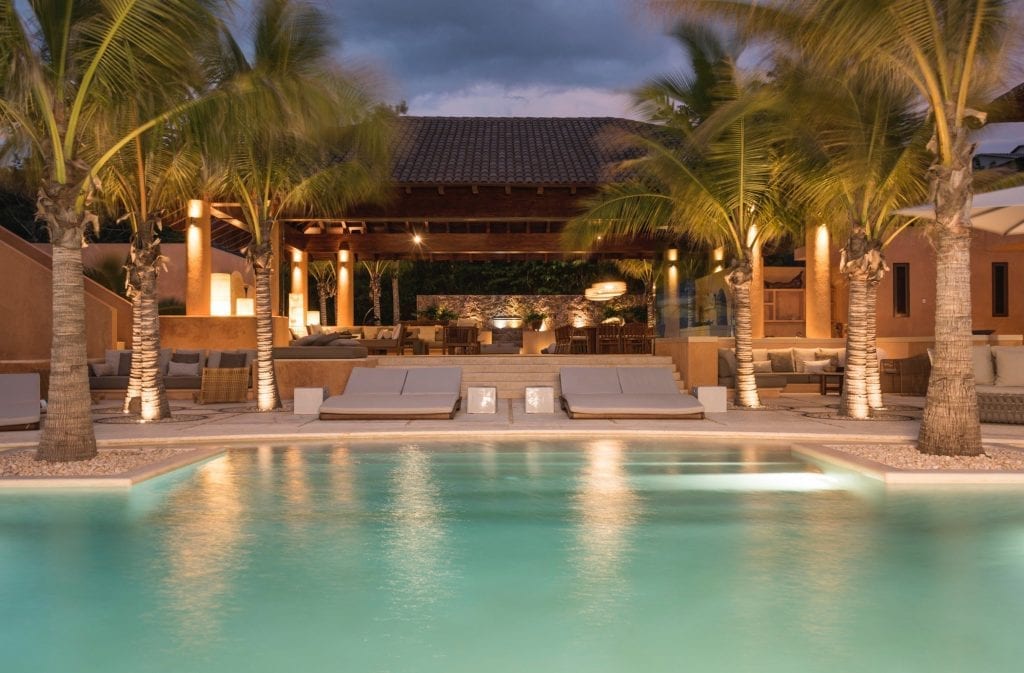 Estate Las Palmas Kupuri 36 the lit pool and palms before the timber-roofed pavilion at dusk — Punta Mita, Mexico