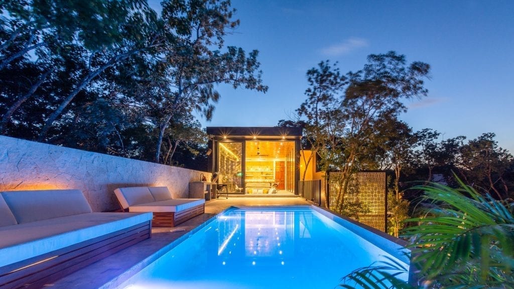 Villa Lagú pool at dusk with cushioned seating and an illuminated pavilion — Tulum, Mexico