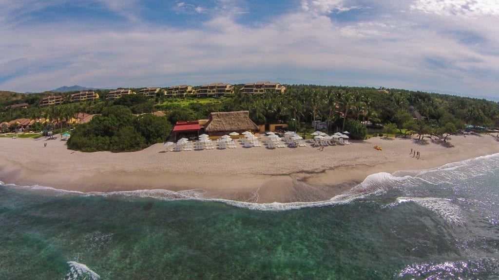 An image showing a luxurious beach club in Punta Mita, Mexico, with elegant lounge chairs and umbrellas on a pristine beach with turquoise waters.