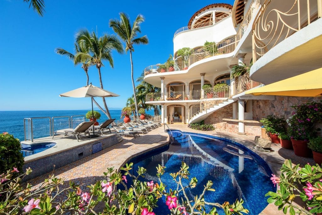 Casa Buena Vida blue pool beside rows of loungers and the curved white villa — Puerto Vallarta, Mexico