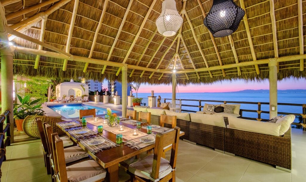 Casa Peregrina dining table and lounge sofas beneath a thatched roof at sunset — Puerto Vallarta, Mexico