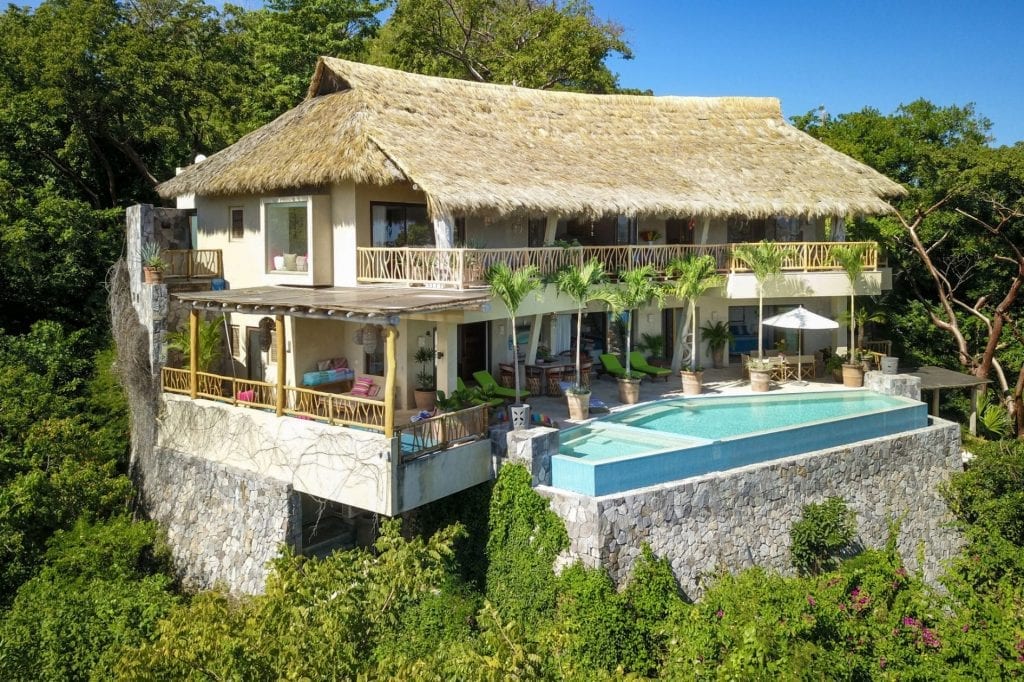 Casa Poseidon elevated villa exterior with a thatched roof and pool above dense greenery — Punta Mita Nayarit, Mexico