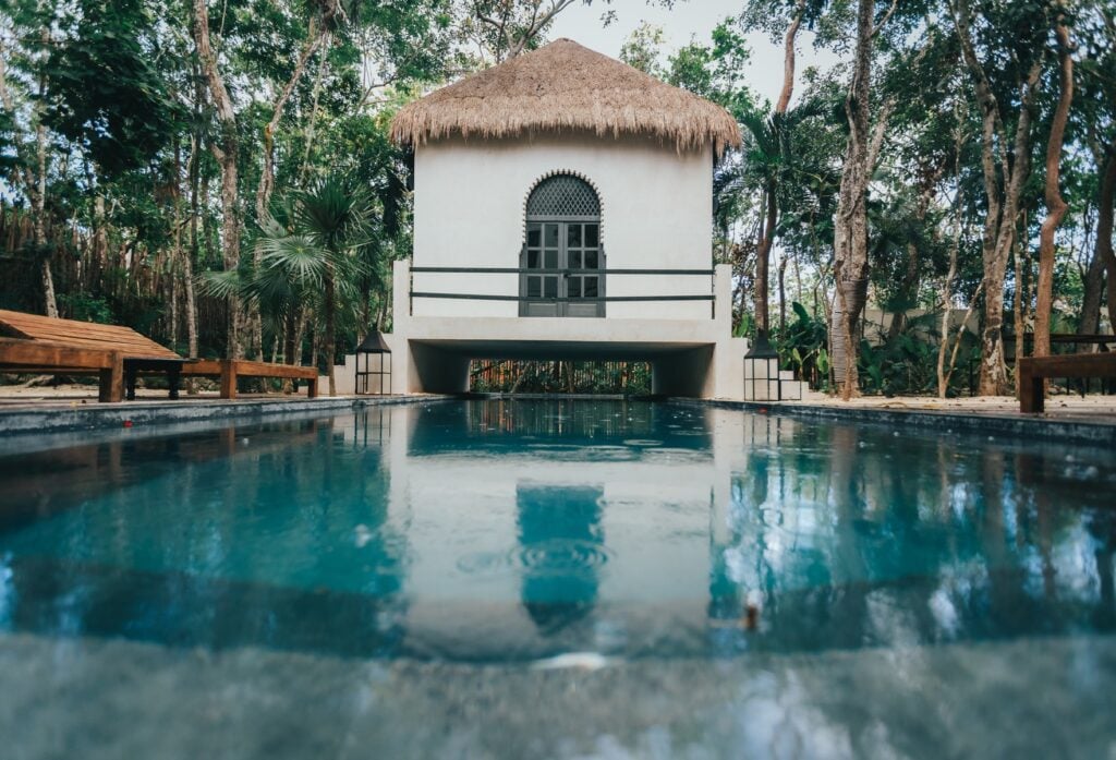Villa Riad Ambre et Epices pool beside a white thatched-roof cabana at the jungle's edge — Tulum, Mexico