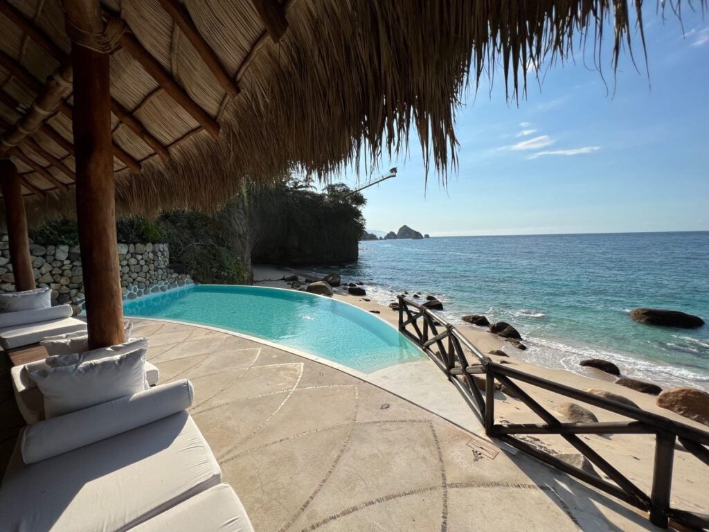 Casa Papelillos el Paredon covered seating beside the curved pool and rocky shore — Puerto Vallarta, Mexico