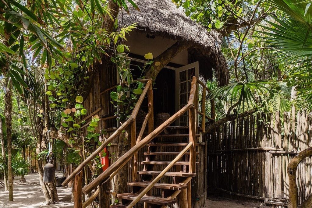 Eclectic Treehouse front exterior with log staircase and wooden fence among palms — Tulum, Mexico
