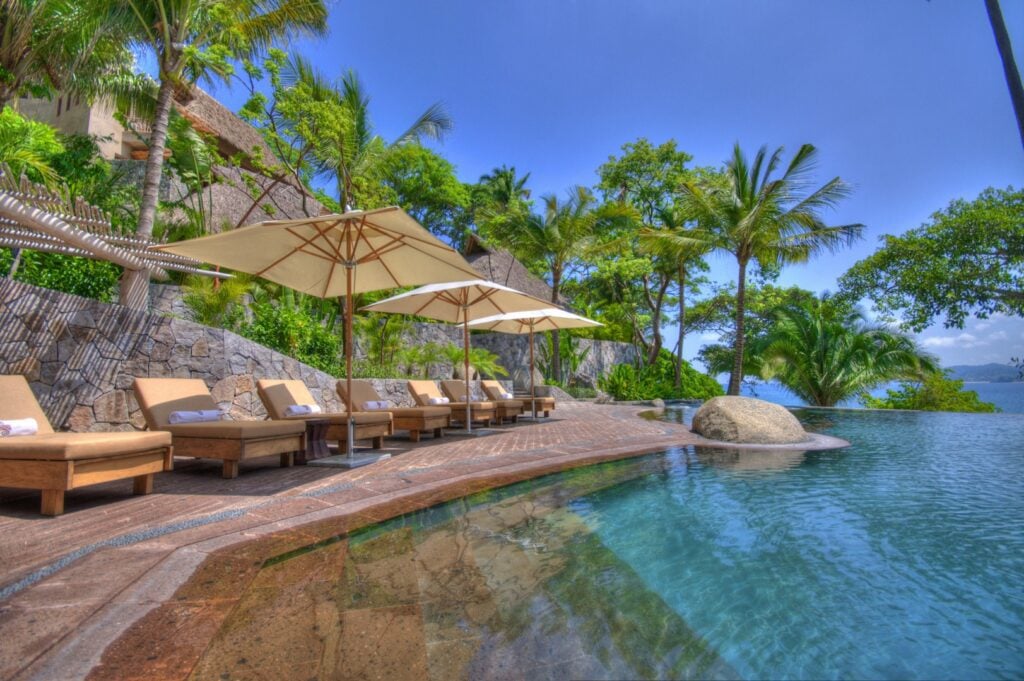 Infinity pool with umbrellas and loungers among palm trees