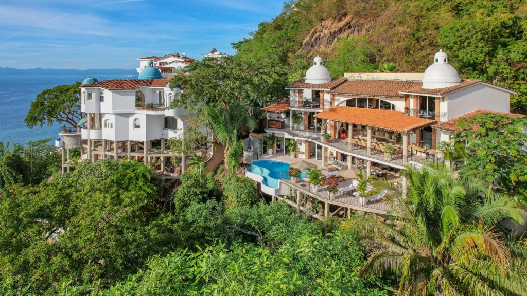 Villa Alexa aerial view of hillside buildings and a curved pool amid trees — Puerto Vallarta, Mexico