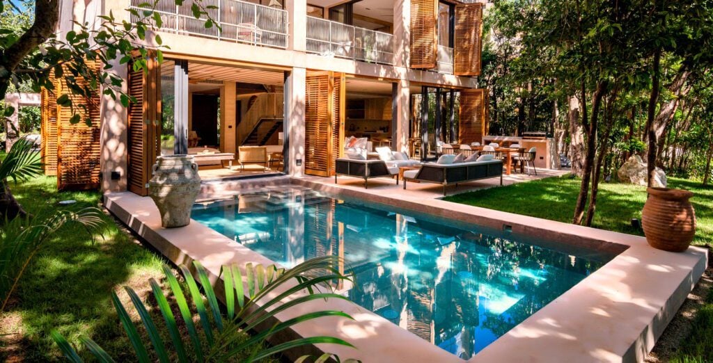 Palm Villa Experience rectangular pool and open facade framed by a palm leaf — Playa del Carmen, Mexico