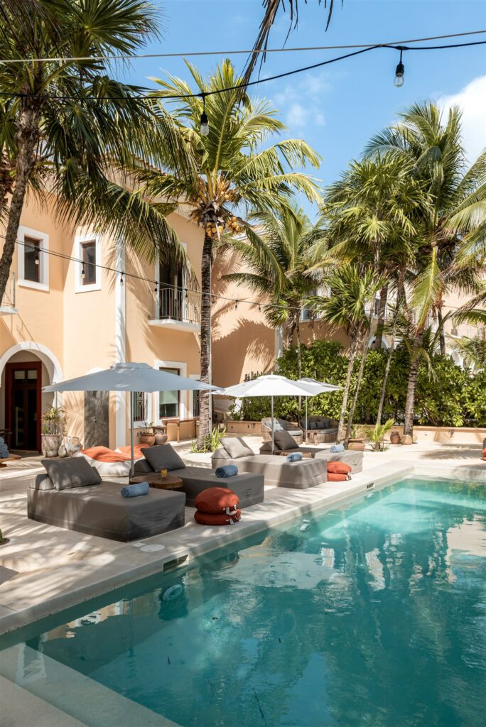 Hacienda Corazon courtyard pool with grey seating, peach facade and tall palms — Puerto Aventuras, Mexico