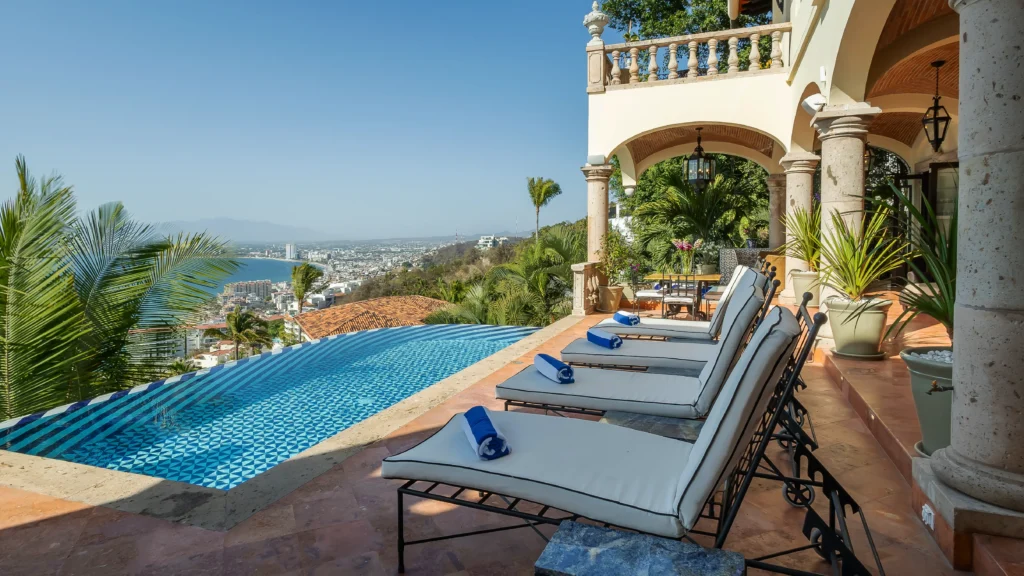 Hacienda de Los Santos poolside terrace with loungers and a hillside bay view — Puerto Vallarta, Mexico