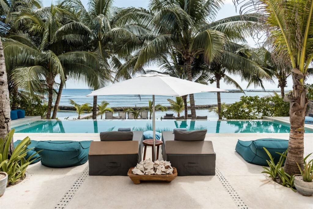 Hacienda del Mar two cushioned loungers beneath an umbrella facing the pool and sea — Puerto Aventuras, Mexico