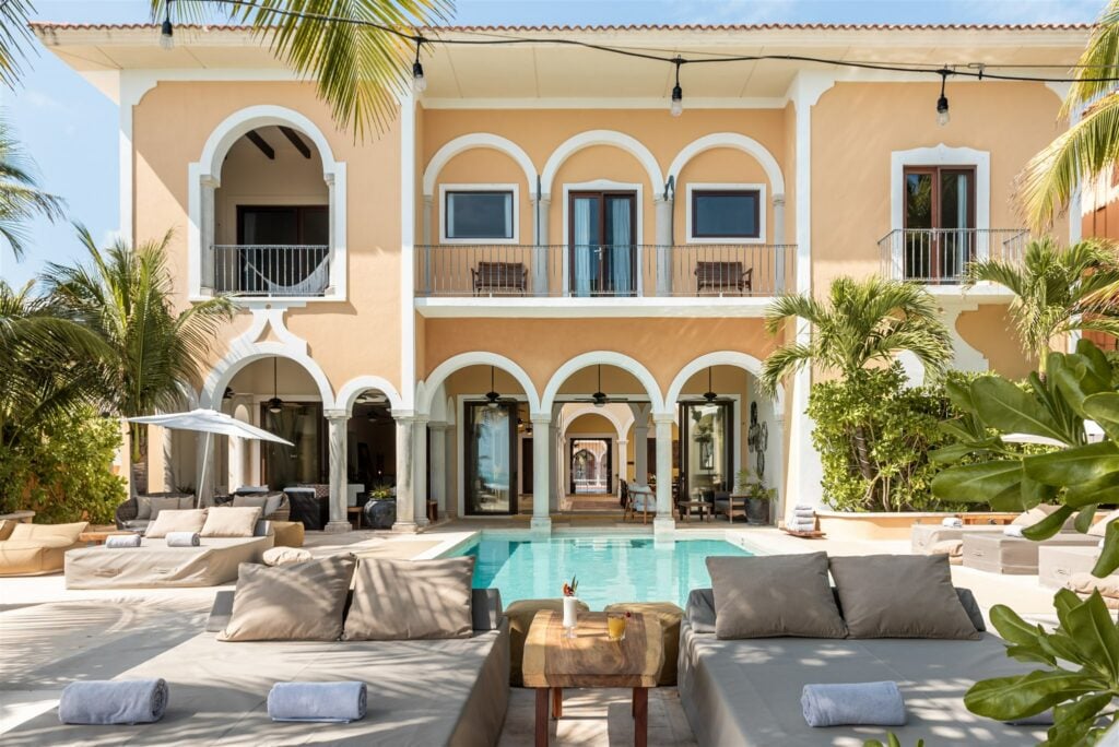 Hacienda Magica daybeds and a rustic table beside the courtyard pool under the arches — Puerto Aventuras, Mexico