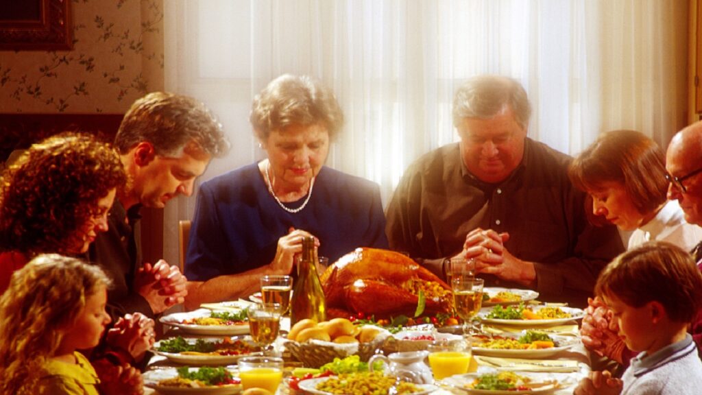 A diverse family of various ages and ethnicities sitting around a Thanksgiving dinner table, enjoying a festive meal with traditional decorations and dishes in a cozy, homey setting.