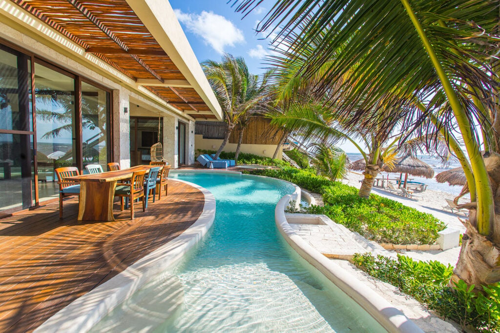 Casa Ha poolside dining terrace with a wood table beside the curved pool — Tulum, Mexico