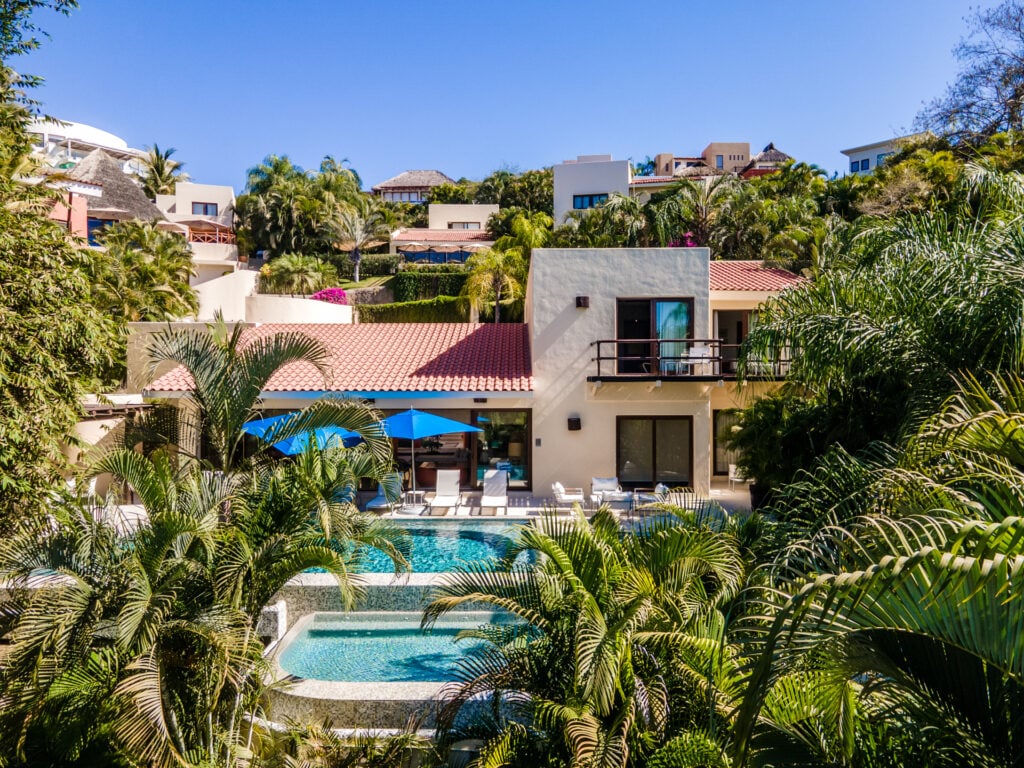 Casa Patio hillside view of the exterior, pools and blue umbrellas among palms — Punta Mita Nayarit, Mexico