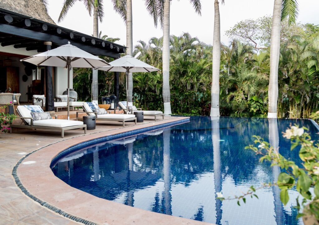 Casa Tres Reinas pool terrace with umbrellas and loungers beneath palms — Punta Mita Nayarit, Mexico