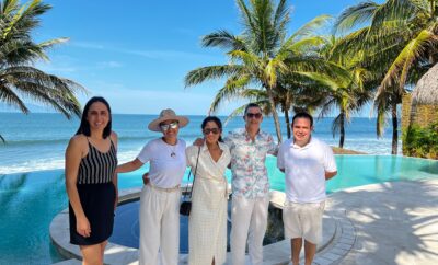 El equipo de Experiencia en la Villa de pie frente a la piscina de una lujosa villa en Punta de Mita, con la playa de fondo.