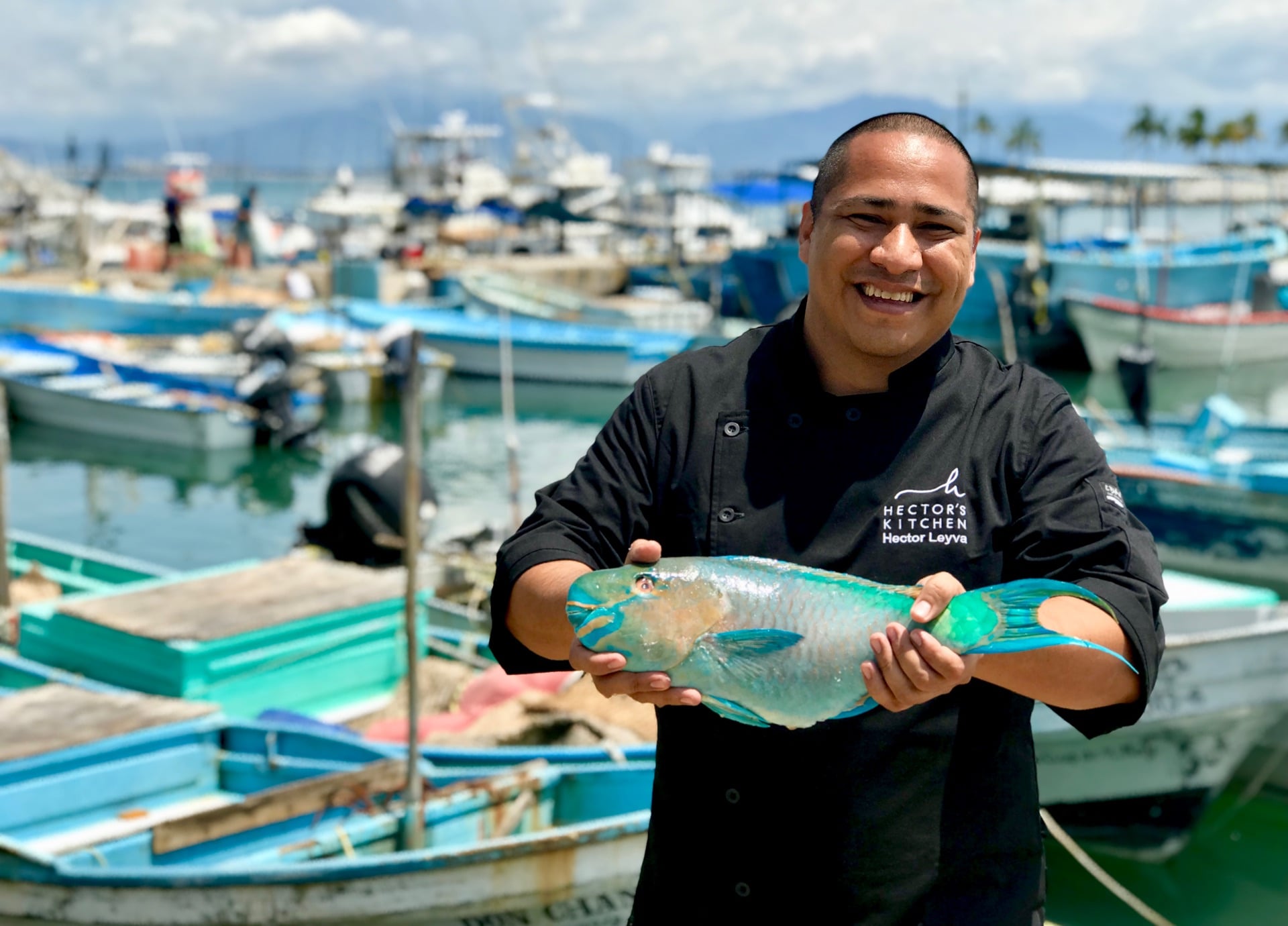 Private chef Héctor Leyva holding a fresh fish beside fishing boats — Punta Mita, Mexico