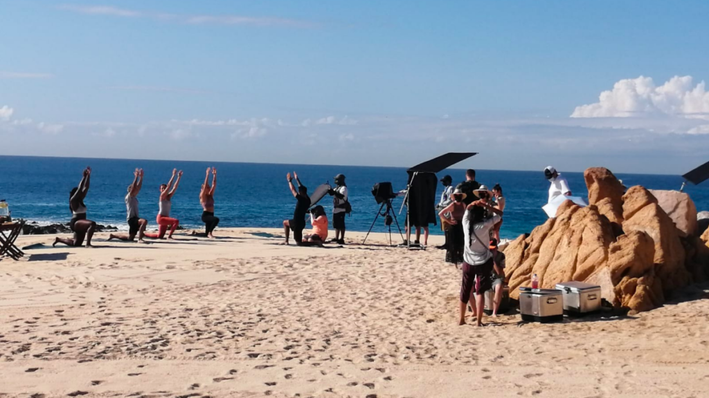 A film crew on the beach in Cabo San Lucas, engaged in a lively on-set filming session.