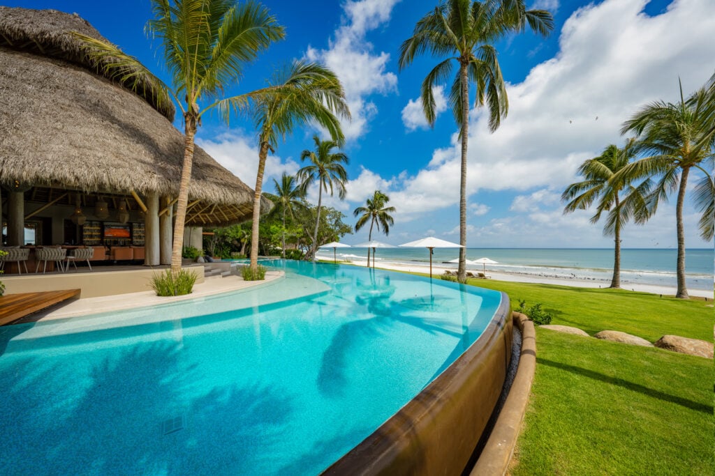 Casa Akama infinity pool with raised wooden lip beside the lawn and beach — Punta Mita, Mexico