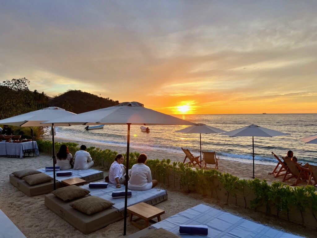 Vacationers relaxing on lounge chairs at Villa Mixto's beachfront terrace, enjoying a stunning sunset over the serene Quimixto Beach.