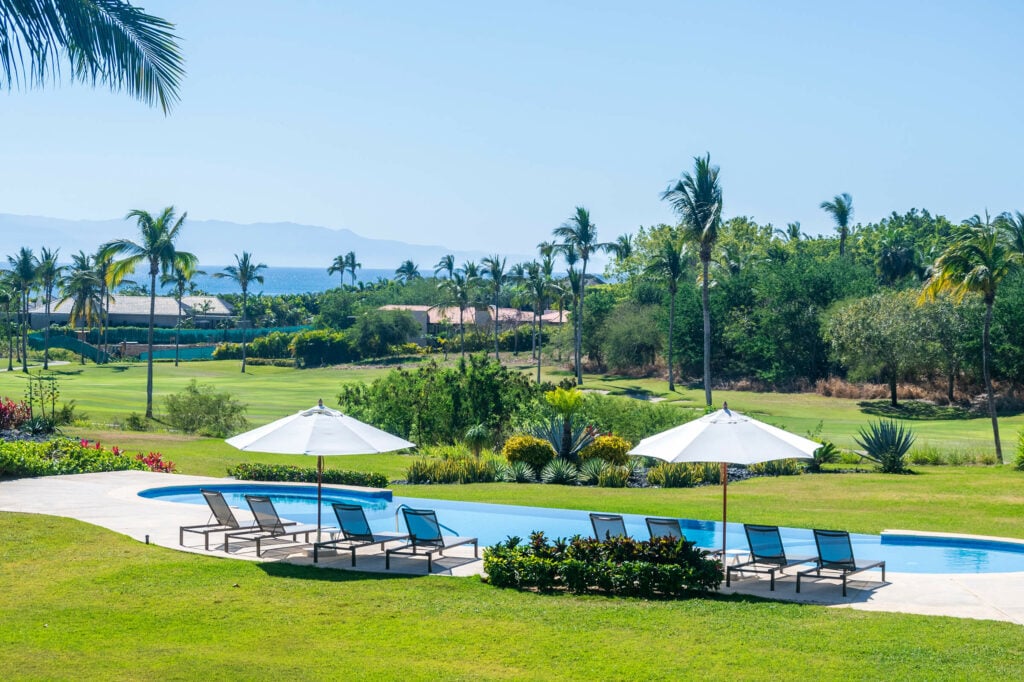Condo Zazil terrace view over a pool, lawns, palm trees and distant water — Punta Mita Nayarit, Mexico