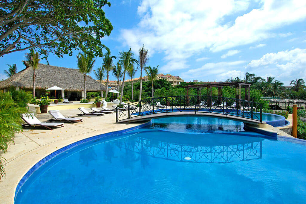Lavish pool area of Hacienda de Mita with the elegant clubhouse in the background, highlighting family-friendly amenities like shaded lounging areas and kid's play zones.