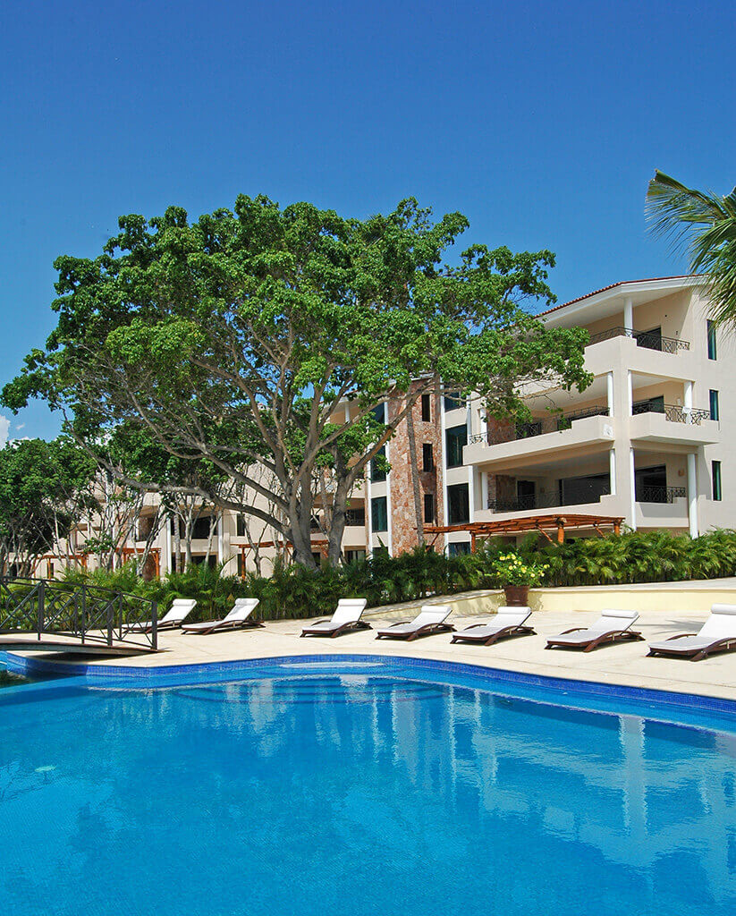 Panoramic view of Hacienda de Mita building alongside its vast beachfront pool, embraced by verdant tropical gardens.