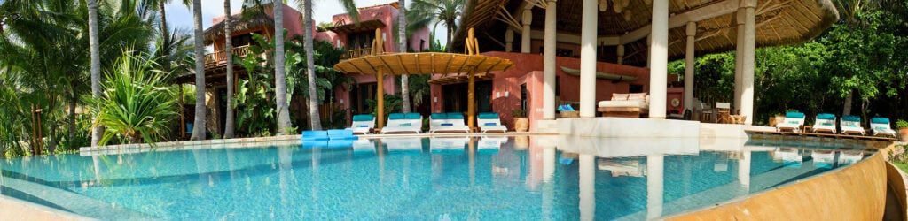 Estate Venado panoramic pool view with a thatched pavilion and pink building — Punta Mita Nayarit, Mexico