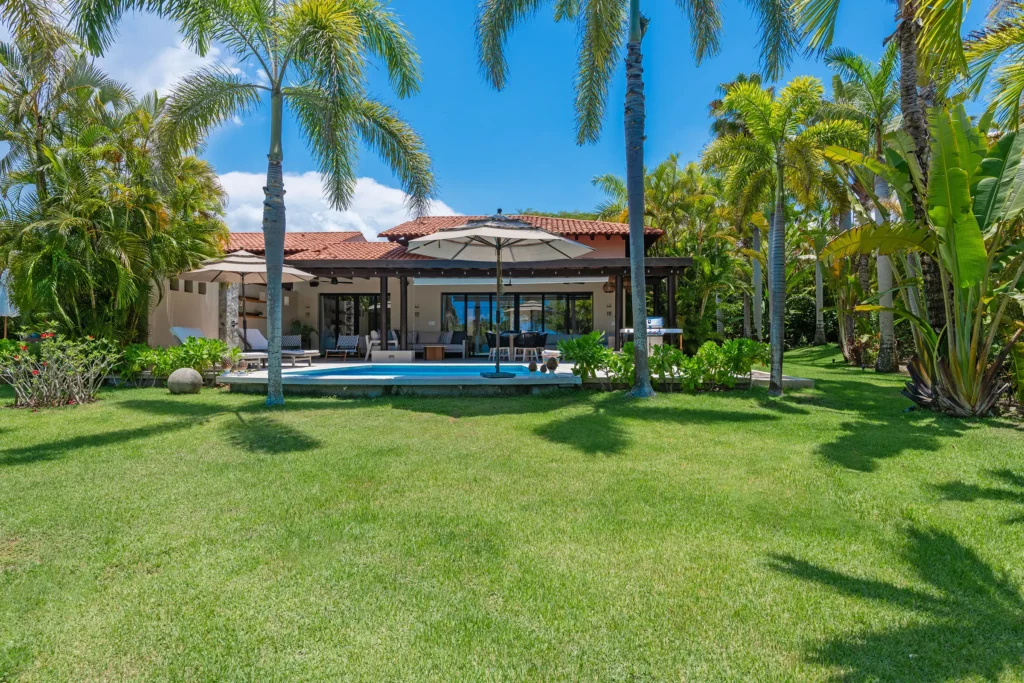 Villa Alfaro in Las Palmas, Punta Mita: tropical villa with red-tiled roof, pool, and patio amid palm trees and blue sky.