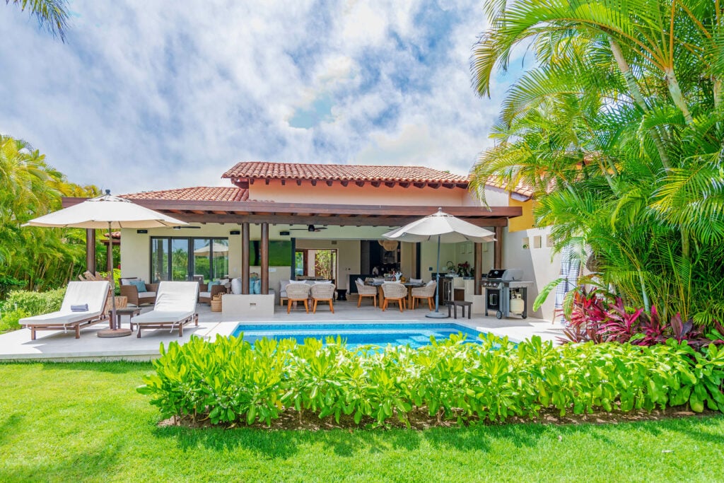 Villa Frida exterior from the lawn with umbrellas, a covered terrace, and swimming pool — Punta Mita Nayarit, Mexico