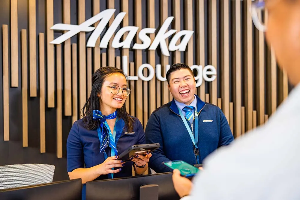 Two Alaska Airlines employees, one male and one female, working diligently at the airline's lounge to provide top-notch service.