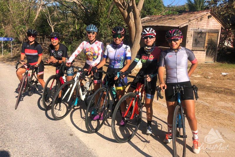 An image showing a group of people on a bike tour in Punta Mita, Mexico, riding along a scenic path with lush greenery and beautiful ocean views.