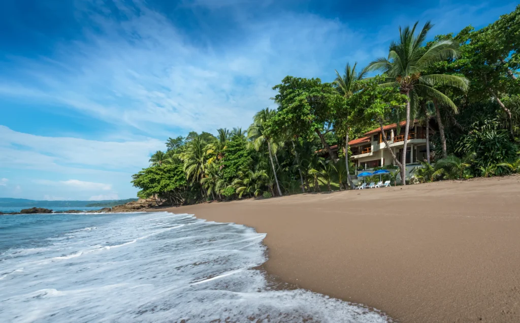 Casa Oceano, nestled among palm trees on Tango Mar beach, Costa Rica, with waves lapping the sandy shore.