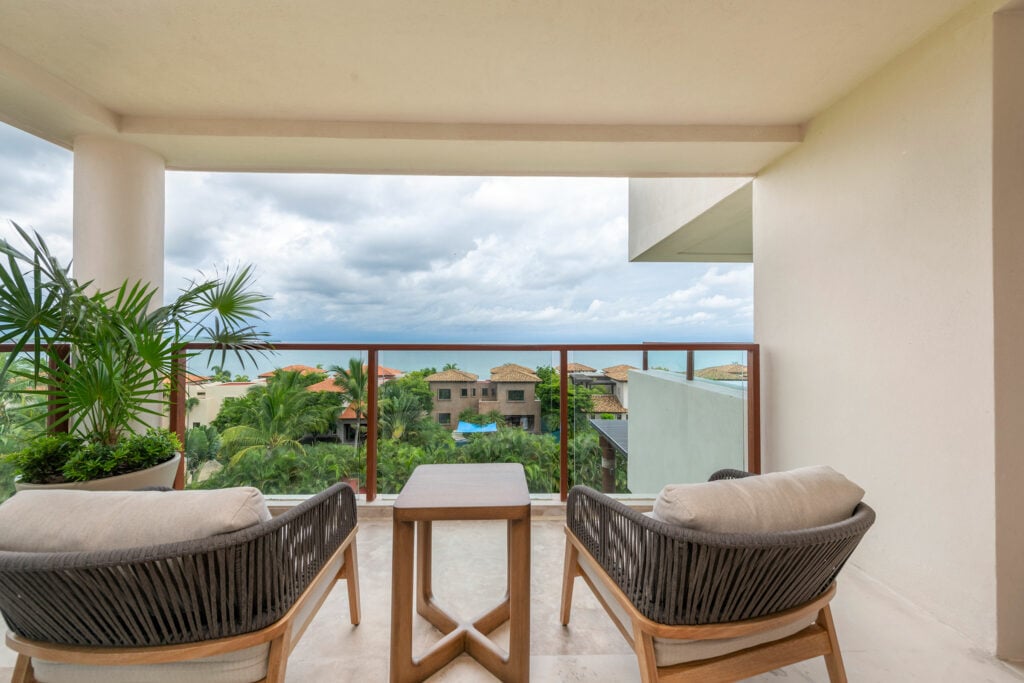 Condo Nautica covered balcony with two wicker chairs overlooking rooftops and ocean — Punta Mita Nayarit, Mexico